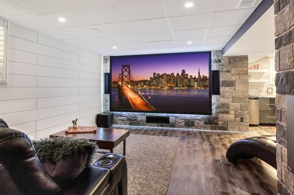 Finished media room with a large screen, stone fireplace surround, and wood-look flooring