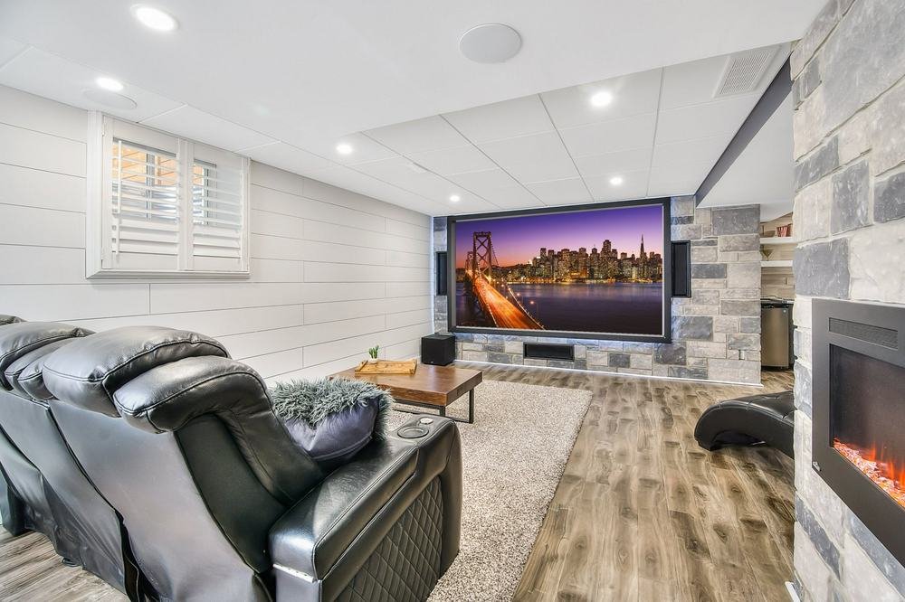 Finished basement media room with projection screen, stone fireplace, and lounge seating