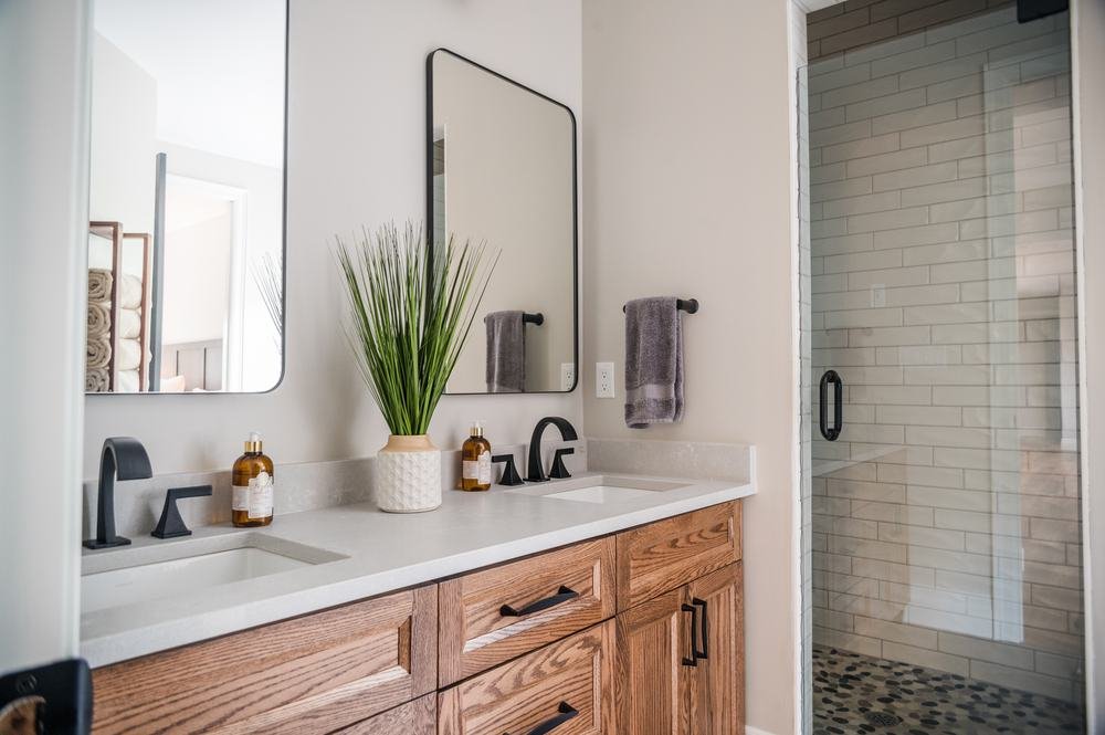 Wood bathroom vanity beside a glass shower with white tile and pebble floor