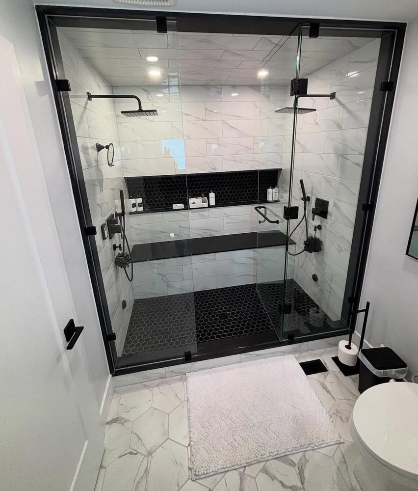 Glass-enclosed shower with large white wall tile and dark fixtures