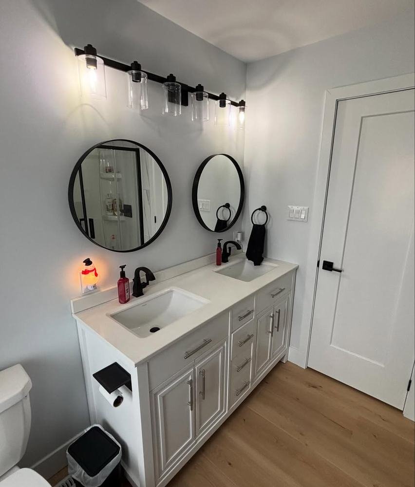 Bathroom vanity wall with double sinks, gray cabinetry, and round mirrors