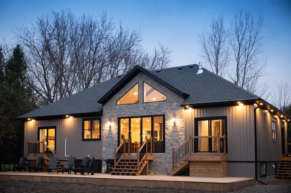 Finished bungalow rear elevation at dusk with illuminated windows and a broad wood deck