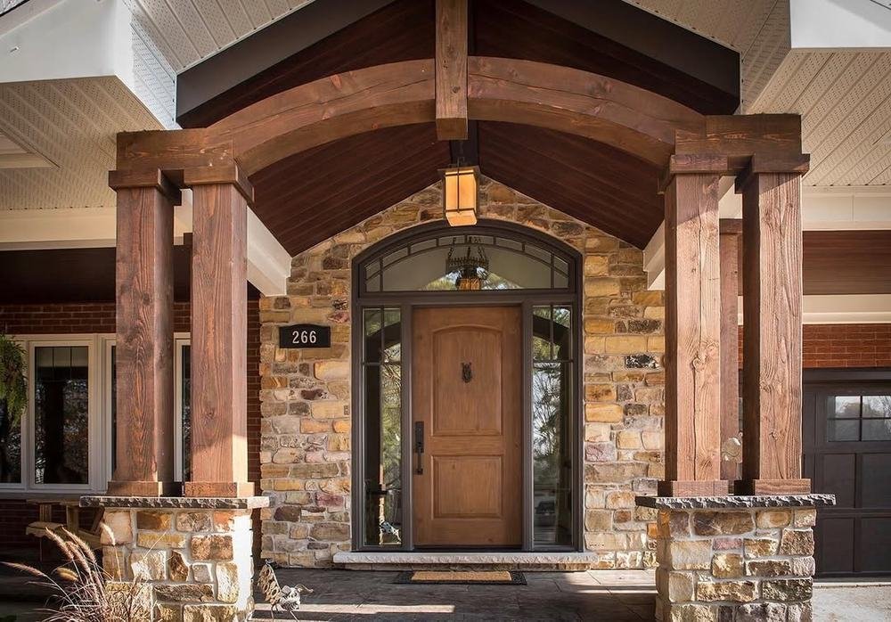 Timber-framed front entrance with stone piers, masonry walls, and wood door