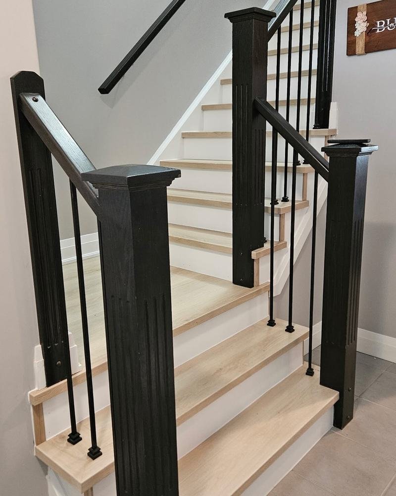 Pale wood staircase with dark posts and metal balusters viewed from the landing