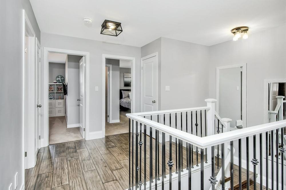 Bright upper hallway with wood-look flooring and a white-and-black stair railing
