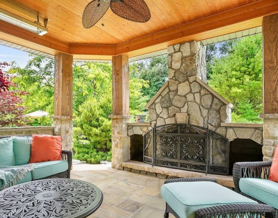Covered outdoor living room with a large stone fireplace and timber ceiling