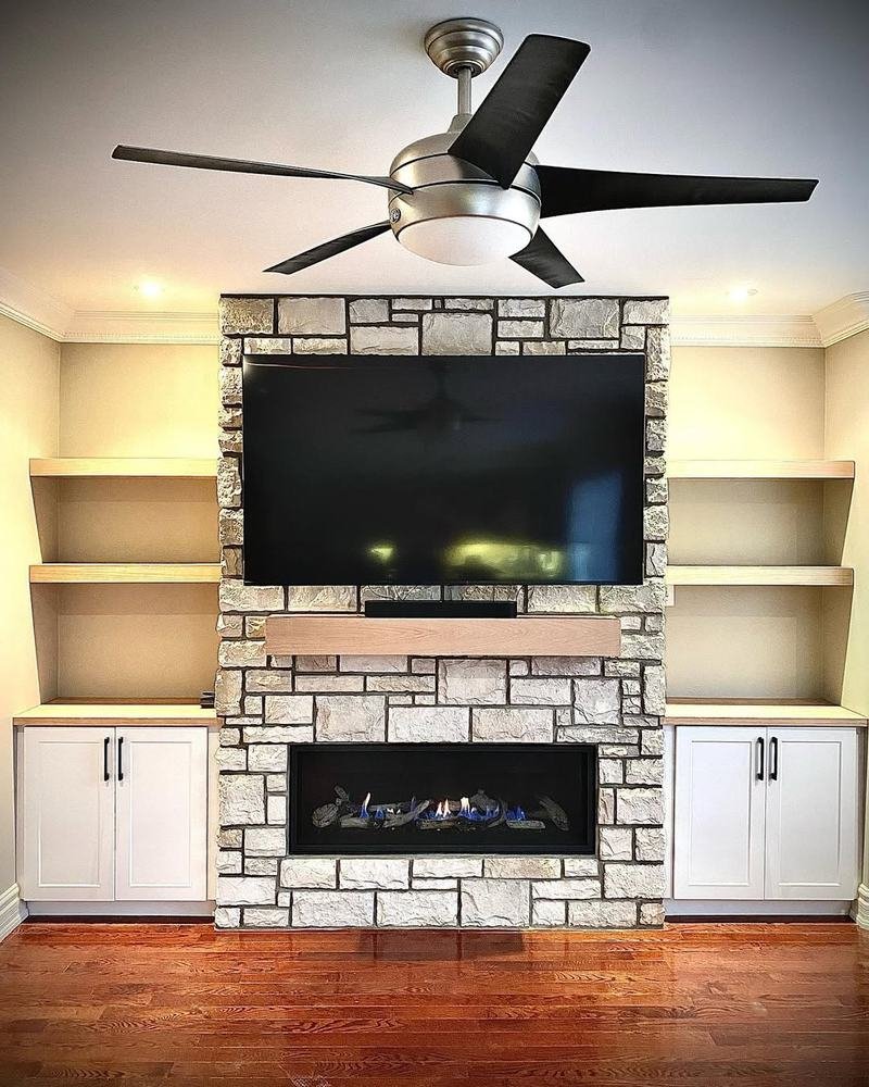 Stone fireplace and television wall flanked by white built-in cabinets and shelves