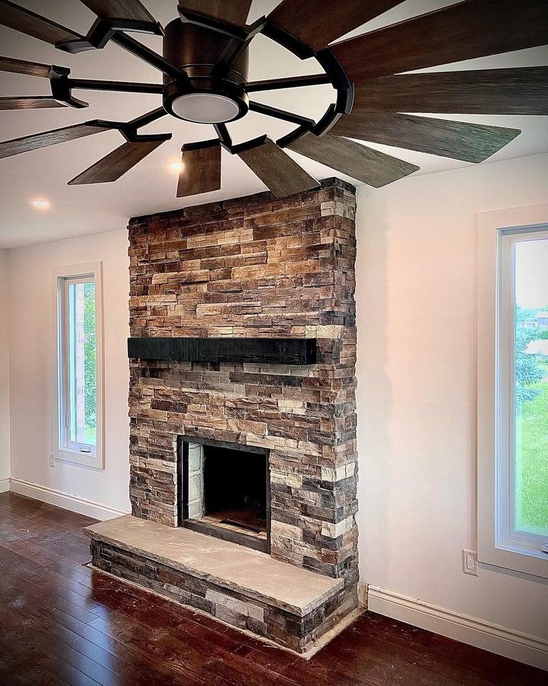 Floor-to-ceiling ledgestone fireplace in a bright room with wood flooring