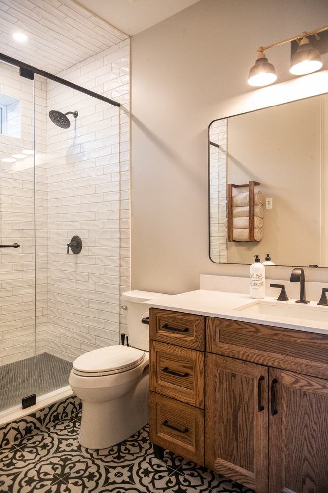 Finished bathroom with wood vanity, glass shower, patterned floor tile, and white wall tile