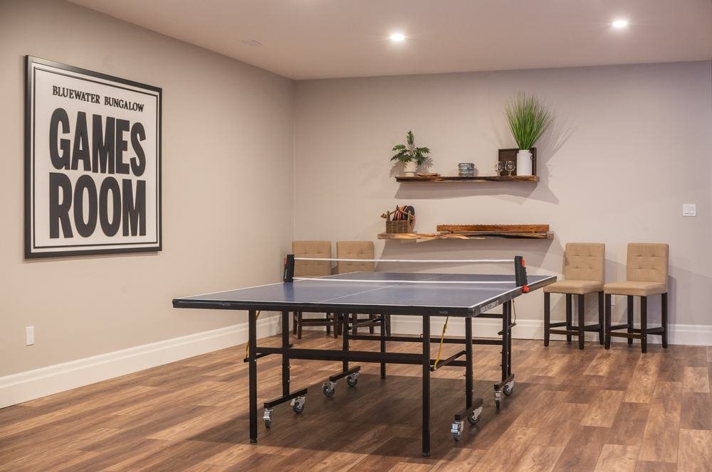 Finished games room with table tennis, wood-look flooring, and open wall shelves