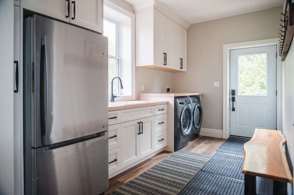 Bright laundry room with white cabinets, wood counter, appliances, and exterior door