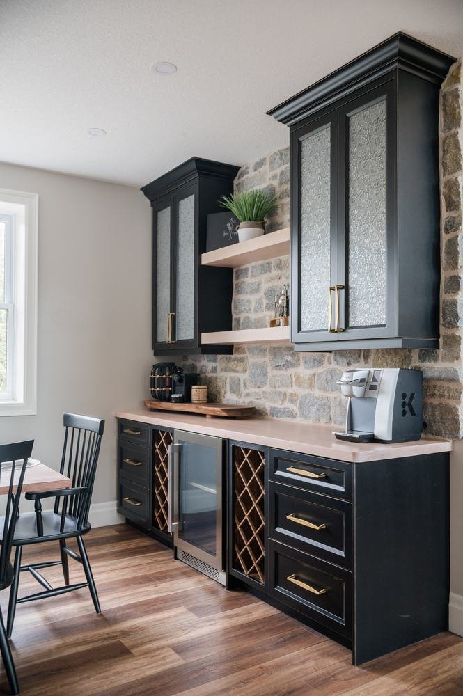 Dark beverage cabinetry and stone backsplash beside a dining area
