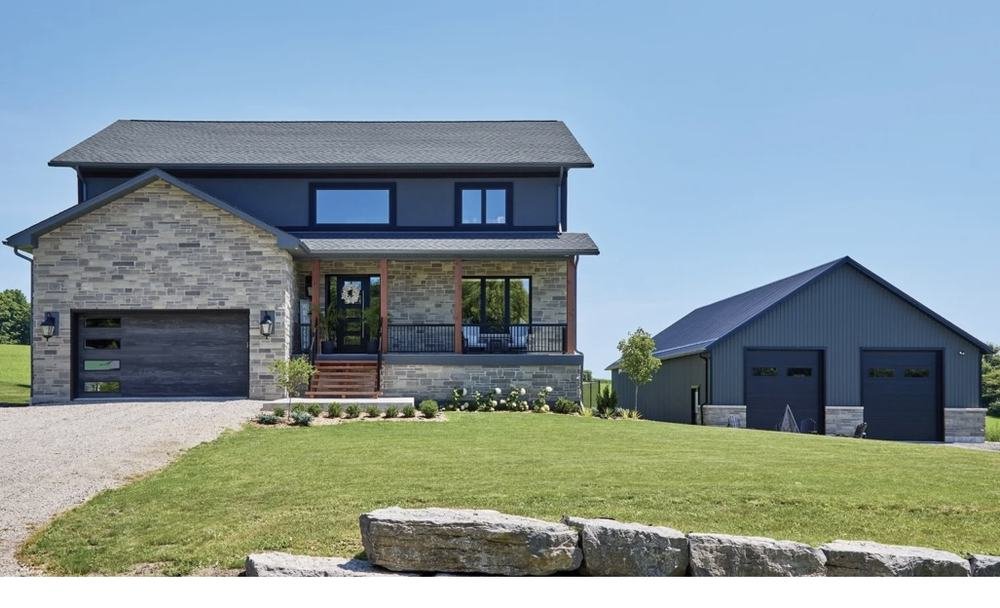 Modern rural home with stone facade, dark siding, and detached outbuilding