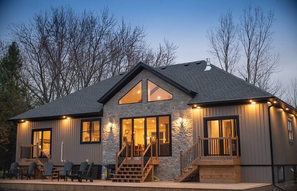 Finished bungalow at dusk with stone accents, deck, and warm interior lights