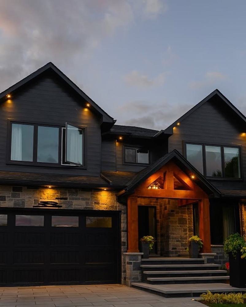 Large home facade with stone cladding, timber entry canopy, and illuminated soffits