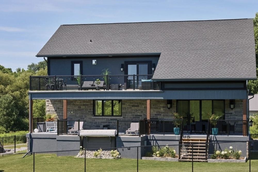 Rear elevation of a dark-sided home with upper balcony and ground-level deck
