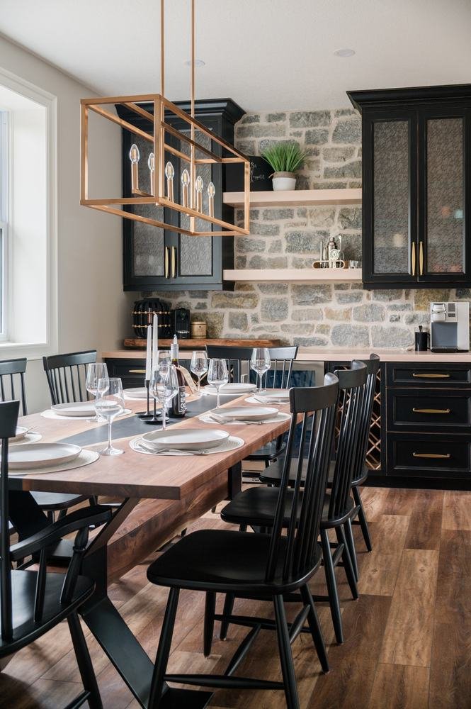 Dining area beside dark kitchen cabinetry and stone backsplash wall