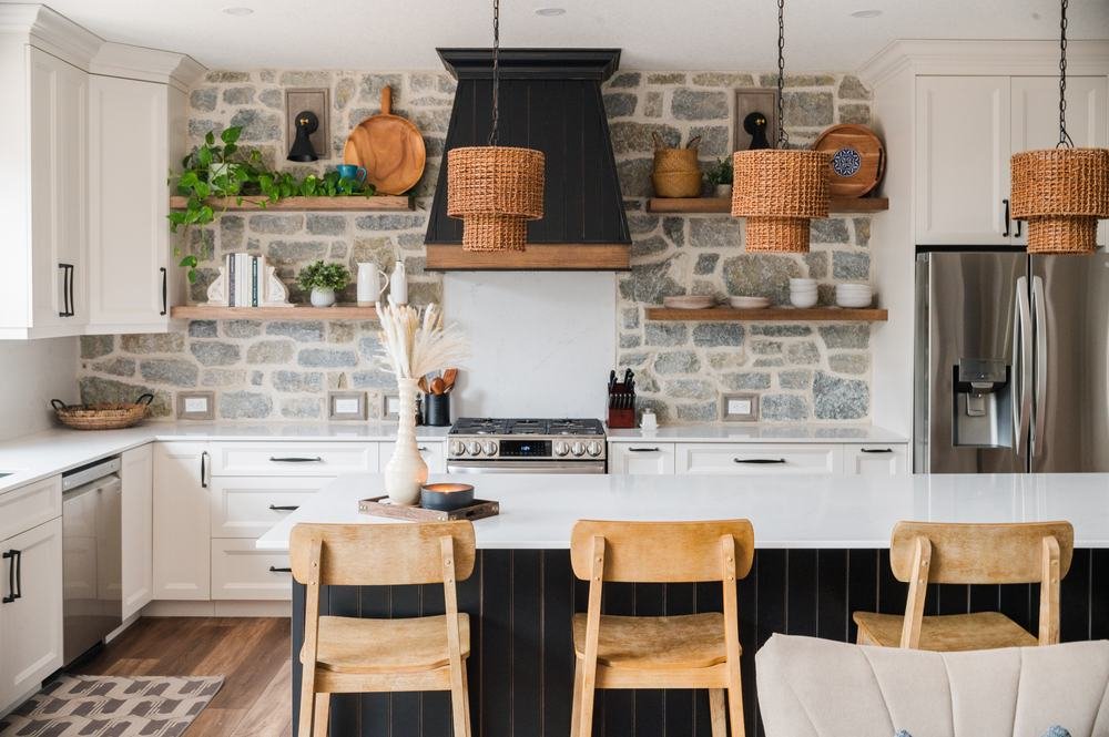 Bright kitchen with a dark island, white cabinetry, pendant lights, and stone backsplash