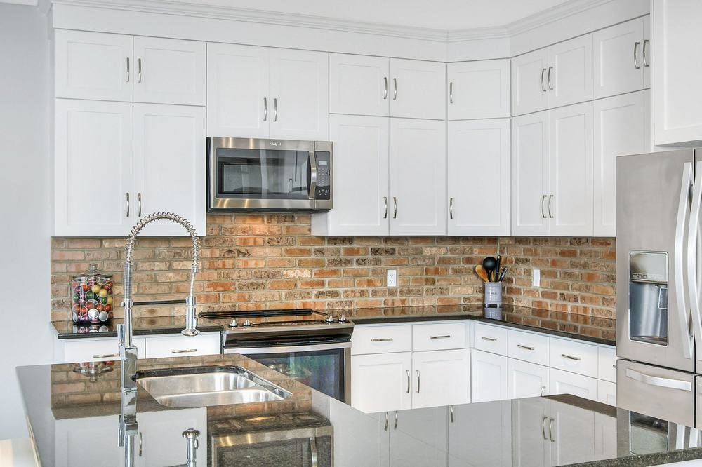 Bright white kitchen with island sink, extensive cabinetry, and brick-pattern backsplash
