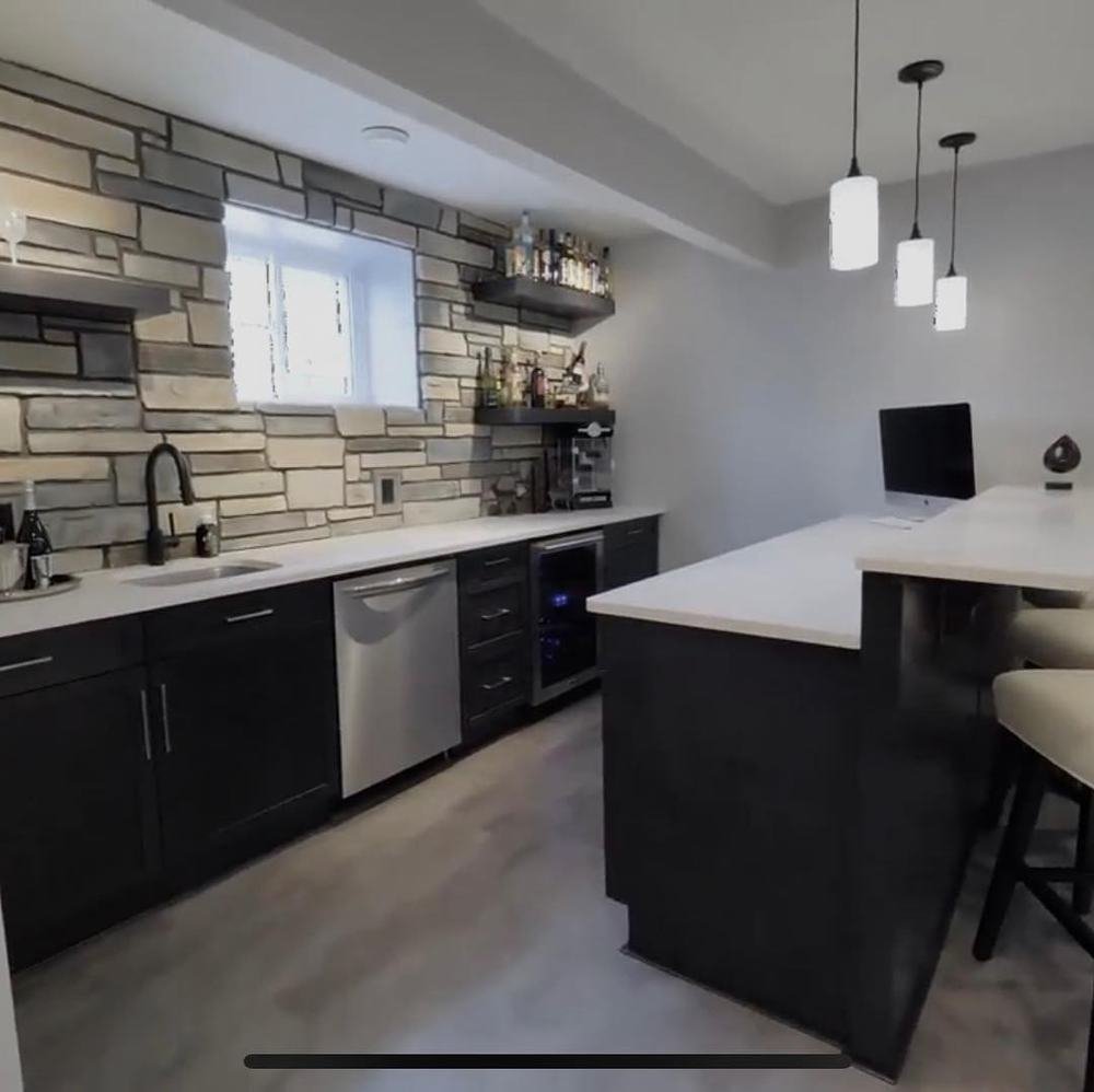 Dark kitchen island and cabinetry beneath a stone backsplash wall