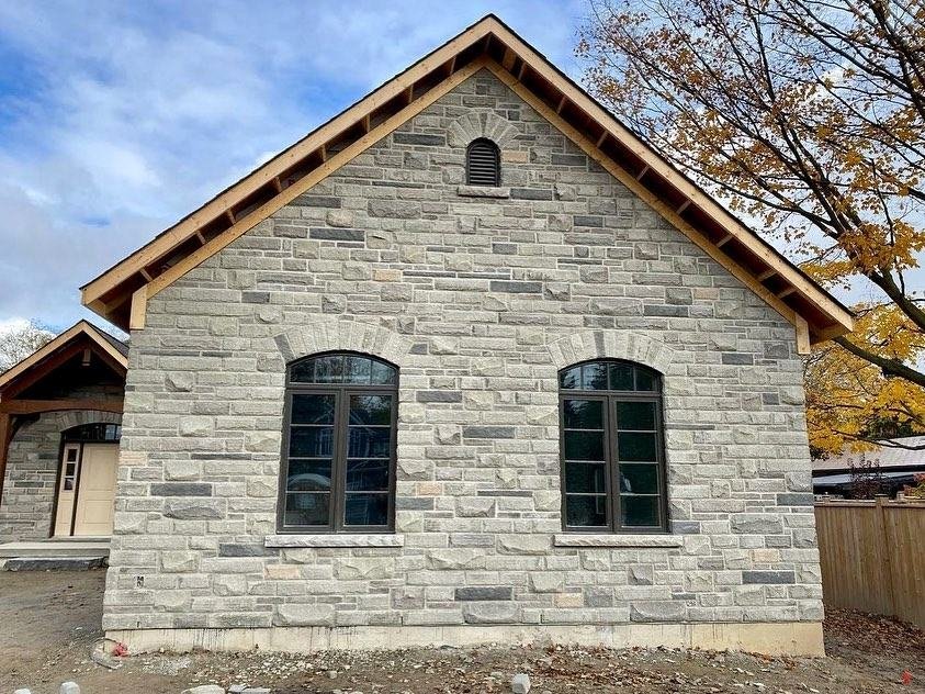 Gabled building clad in light stone with dark arched windows