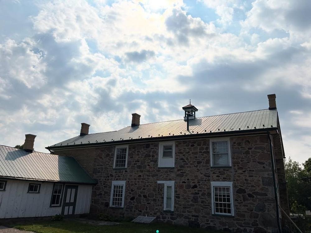 Long historic stone building with metal roof and multi-pane windows