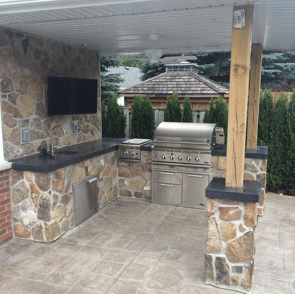 Covered outdoor kitchen with stone supports, grill, counter, and tiled floor